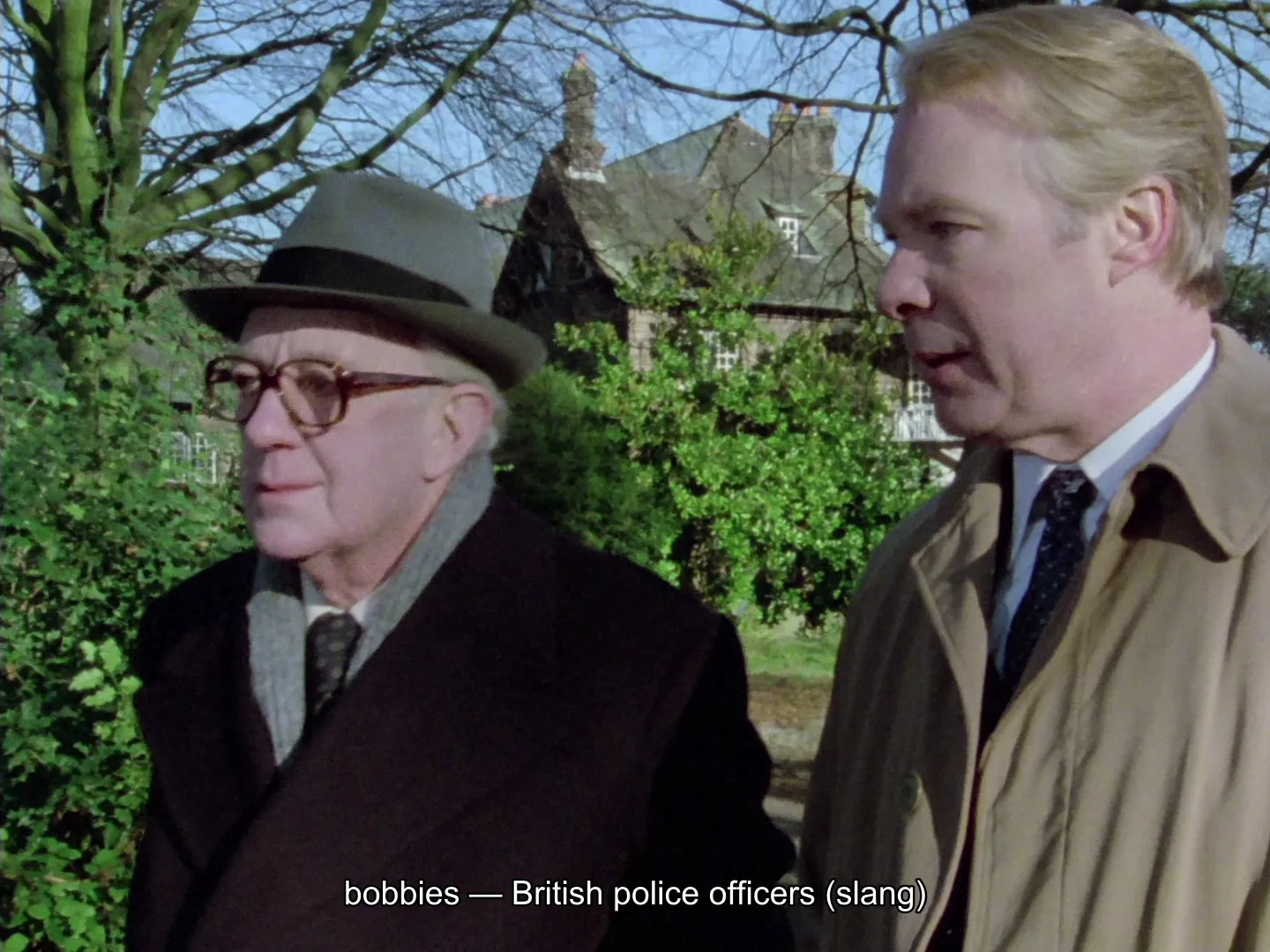 George Smiley out walking with a colleague in Tinker, Tailor, Soldier, Spy (1979), with an Explainer subtitle along the bottom reading “bobbies — British police officers (slang)”